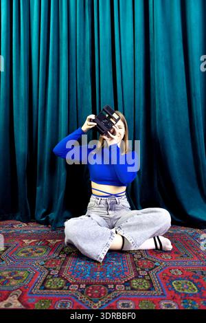 Un adolescente simpatico con abiti casual scatta foto sedute sul tappeto. La ragazza tiene in mano una macchina fotografica retrò e prende un p Foto Stock