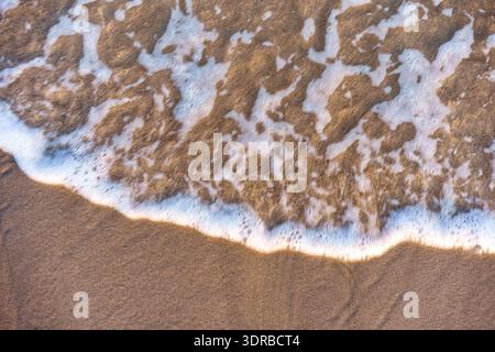 Acqua astratta di mare e dolci onde che scorrono sulla spiaggia di sabbia durante la calda luce del tramonto Foto Stock
