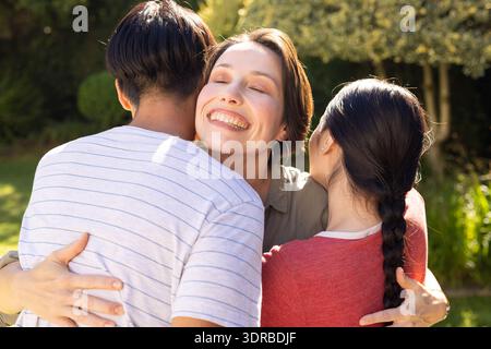 Donna sorridente che abbraccia figli e figli adolescenti, trascorrendo il tempo in famiglia all'aperto insieme Foto Stock