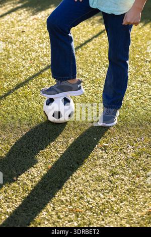 Giocare a calcio, uomo asiatico di mezza età in piedi su un campo di erba con piede su un pallone da calcio, all'aperto Foto Stock