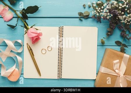 Collezione di articoli su un tavolo blu con fiori rosa, anelli d'oro e una confezione regalo Foto Stock