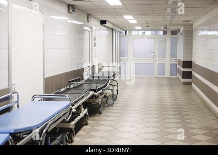 Corridoio ospedale vuoto con letti medici lungo il muro. Interno pulito e moderno della clinica con illuminazione luminosa, barelle di emergenza e atmosfera sterile Foto Stock