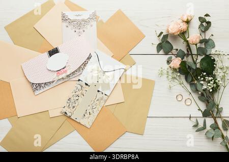 Collezione di inviti nuziali e composizioni floreali su una superficie in legno chiaro Foto Stock