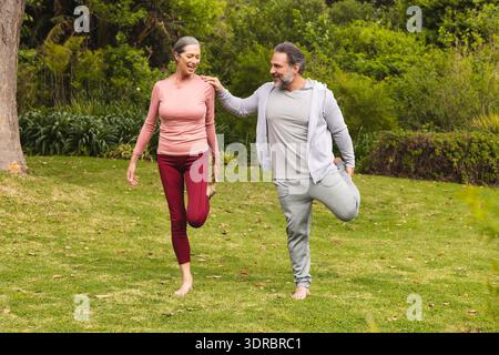 Coppia matura che si diverte ad allenarsi all'aperto insieme, bilanciandosi su una gamba nel parco Foto Stock