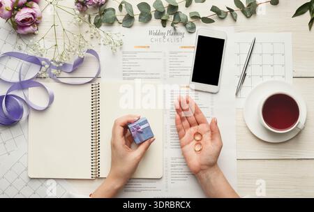 Raccolta di elementi di pianificazione matrimonio su un tavolo con anelli e lista di controllo Foto Stock