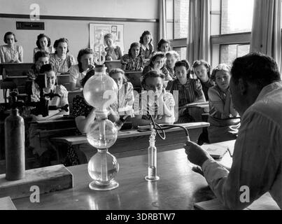 Questa fotografia mostra una lezione di chimica al liceo delle ragazze cattoliche a l'Aia, nei Paesi Bassi, il 3 ottobre 1940 durante la seconda guerra mondiale. Gli studenti sono impegnati in istruzione scientifica, osservando esperimenti e partecipando ad attività in classe. L'immagine documenta le pratiche educative olandesi, gli interni della scuola, le attrezzature da laboratorio, l'apprendimento degli studenti e la continuazione della scuola in condizioni di guerra. Foto Stock