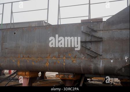 Primo piano del lato in acciaio di una nave con rinforzi saldati. Sezione metallica dello scafo di una nave montata su supporti temporanei durante il montaggio in fabbrica. Foto Stock