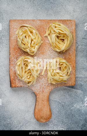 Tagliatelle. Pasta tradizionale italiana cruda fatta in casa su una tavola di legno su fondo grigio di cemento. Messa a fuoco selettiva Foto Stock