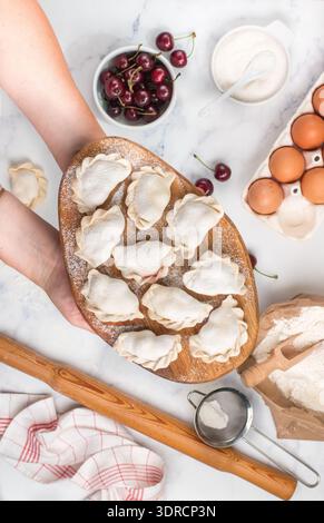 Preparare deliziosi gnocchi dolci con ciliegie. Dessert tradizionale russo e ucraino. Vareniki e gli ingredienti sulla marba Foto Stock