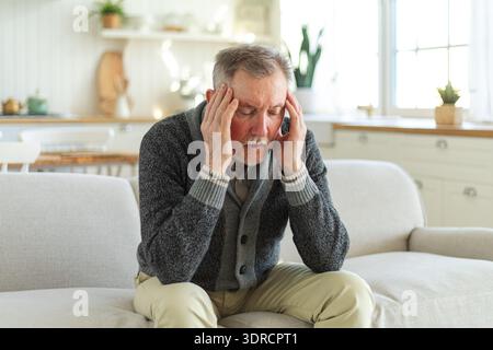 Mal di testa dolore. Infelice anziano di mezza età che soffre di mal di testa malato che sfrega templi a casa. Vecchio nonno anziano maturo Foto Stock