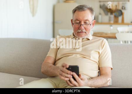 Uomo anziano felice di mezza età che tiene in mano utilizzando lo smartphone touch screen digitando la pagina di scorrimento. Elegante, vecchio nonno di barba matura wi Foto Stock