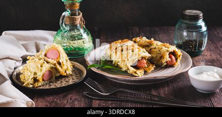 Salsicce avvolte in pancake di cavolo grattugiati su un piatto su un banner da tavolo Foto Stock