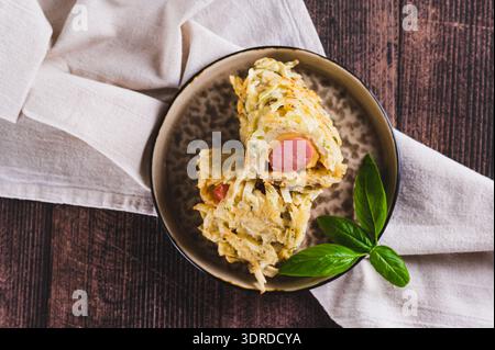 Primo piano di salsicce avvolte in pancake di cavolo tagliati su un piatto con vista dall'alto del tavolo Foto Stock