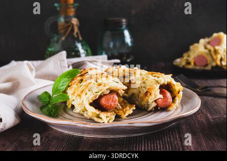Salsicce avvolte in pancake di cavolo grattugiati su un piatto su un tavolo Foto Stock