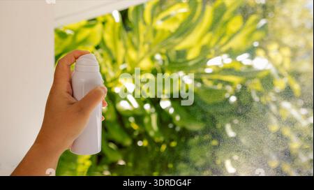 Primo piano di una donna che spruzza il liquido da una bottiglia bianca. La donna usa l'acqua termale. Un modello pulito di un vasetto di acqua ag Foto Stock