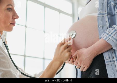 Medico che esamina la donna incinta che tiene lo stetoscopio vicino alla pancia grande che ascolta il battito cardiaco del bambino. Ginecologo medico consulenza pati Foto Stock