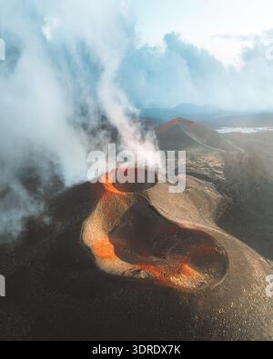 Vista aerea del paesaggio vulcanico con fumo che sale dal cratere, in contrasto con il terreno aspro, Nicolosi, Sicilia, Italia. Foto Stock