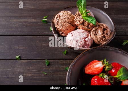 Ciotole di gelato e fragole fresche poste su un tavolo di legno Foto Stock