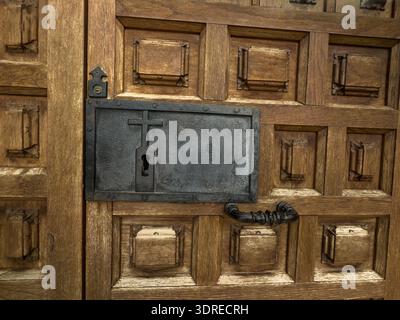 Dettaglio di una porta in legno con serratura in ferro a forma di croce e pannelli scolpiti su una chiesa storica Foto Stock