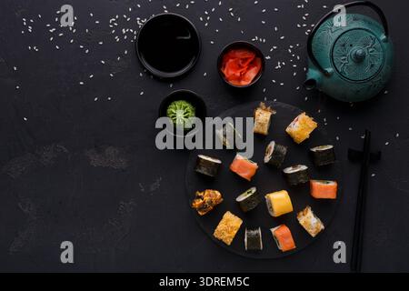 Collezione di sushi esposta su una superficie scura con teiera e condimenti per un'esperienza culinaria Foto Stock