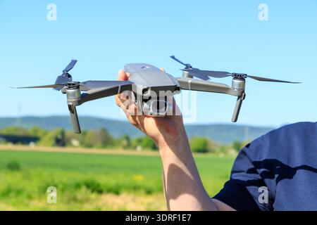 Uomo che tiene in mano il drone prima dell'inizio del volo sullo sfondo del campo e del cielo blu. Hobby all'aperto. Foto Stock