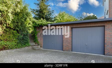 Moderno parcheggio in una casa residenziale in mattoni per auto con persiane grigie sui cancelli. Porte chiuse nei garage. Foto Stock