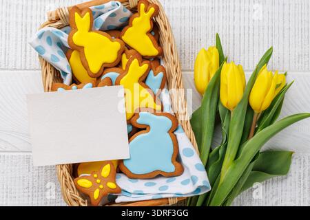 Biscotti di pan di zenzero a forma di coniglietto pasquale, tulipani gialli e biglietto d'auguri Foto Stock