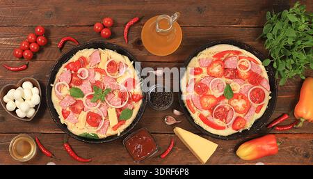 Pizza con prosciutto in padelle di ghisa, con pomodori, limone, mozzarella, salsa, basilico e formaggio su sfondo in legno. moderna panetteria Foto Stock