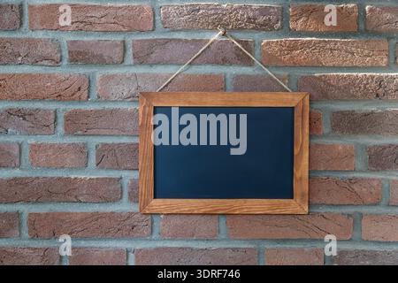 Lavagna nera vintage vuota o lavagna scolastica, cornice del menu o mockup di carte appeso sullo sfondo della parete in mattoni. Lavagna marrone in legno con spazio di copia. Foto Stock