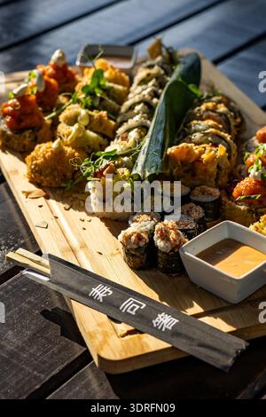 Un delizioso e ben organizzato piatto di sushi roll giapponesi assortiti serviti su un grande tavolo di legno. Il set include una varietà di maki, uram Foto Stock