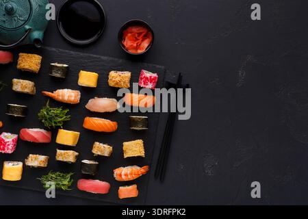 Collezione di diversi tipi di sushi organizzata su una tavola da servizio nera con condimenti Foto Stock