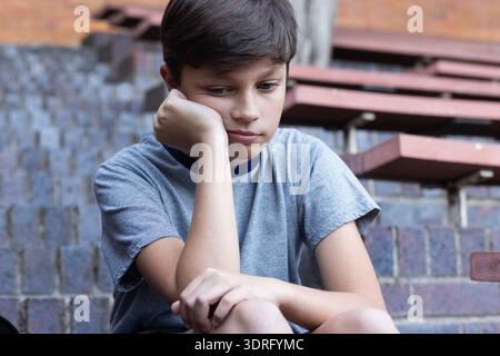 Seduto sui gradini, ragazzo che sembra triste e premuroso a scuola. Bambini, emozioni, tristezza, contemplazione, solitudine, riflesso Foto Stock