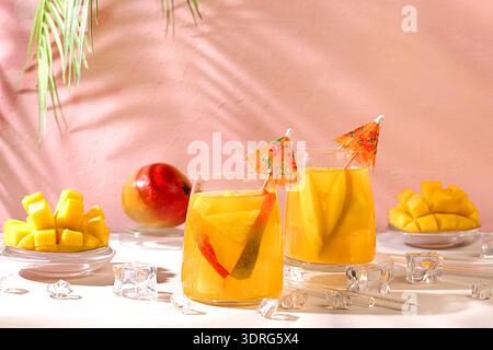 Cocktail fatto in casa, succo di frutta o limonata con fette di mango e ghiaccio sul soleggiato tavolo da cucina. Concetto di festa estiva. Rinfrescante estate Foto Stock