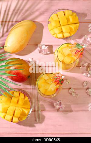 Concetto di festa estiva. Cocktail fatto in casa, succo di frutta o limonata con fette di mango e ghiaccio sul soleggiato tavolo da cucina. Rinfrescante estate Foto Stock