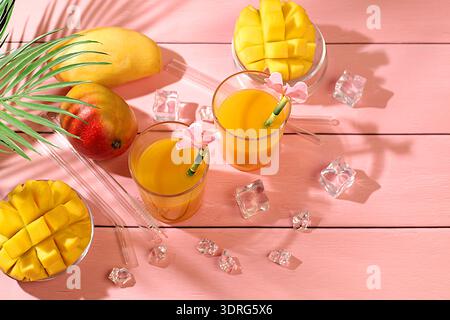 Concetto di festa estiva. Cocktail fatto in casa, succo di frutta o limonata con fette di mango e ghiaccio sul soleggiato tavolo da cucina. Rinfrescante estate Foto Stock