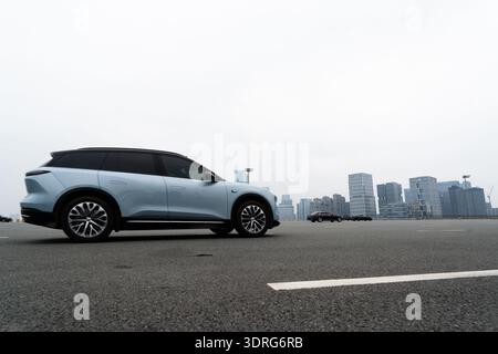 Moderno SUV elettrico parcheggiato sull'autostrada con lo skyline della città sullo sfondo sotto il cielo coperto Foto Stock