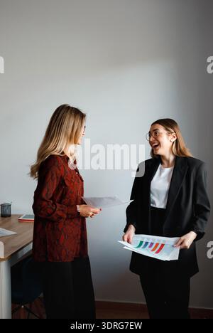 Due donne si impegnano in una conversazione sui rapporti di lavoro mentre si trovano in ufficio. Hanno documenti e condividono idee. Foto Stock