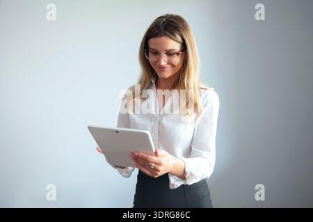 Una donna si trova in un ufficio mentre utilizza un tablet e sorride mentre si occupa delle sue attività al lavoro. Foto Stock