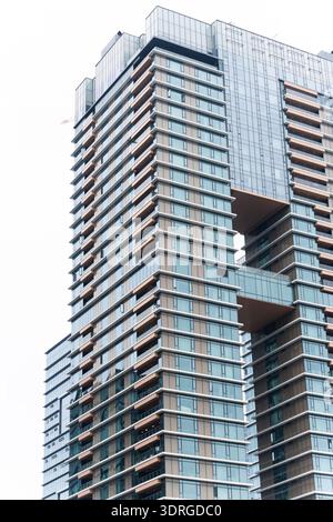 Moderno ed alto edificio di appartamenti con facciata in vetro e balconi in legno nel paesaggio urbano Foto Stock
