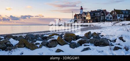 Il tramonto invernale illumina l'idilliaco villaggio sul mare con il faro vicino alle acque calme Foto Stock