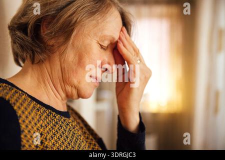 Primo piano di una donna anziana che soffre di mal di testa. La signora matura ha chiuso gli occhi e tiene la fronte con la mano Foto Stock