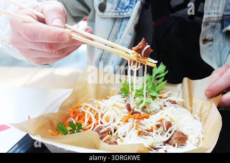 Tizio che mangia spaghetti con bacchette di manzo. Foto Stock