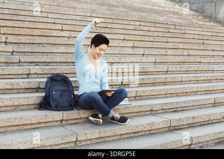 Giovane che si diverte a studiare sulle scale all'aperto in una giornata di sole Foto Stock