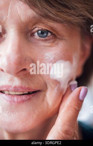 Primo piano del viso di una donna anziana con idratante sulla guancia Foto Stock