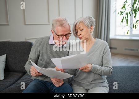 Triste stanca e delusa, la coppia di anziani di mezza età si siede con un documento cartaceo. Infelice anziano uomo maturo donna che legge carta Bill mana Foto Stock