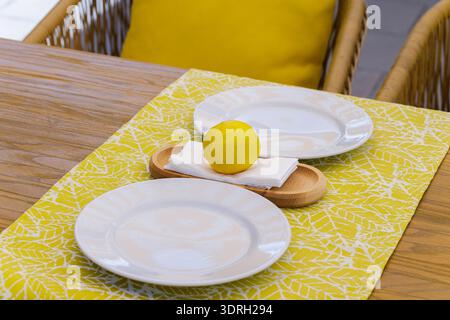 Tavolo con un solo limone su un canale a foglia gialla e piatti bianchi Foto Stock