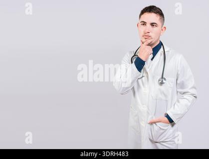 Un medico pensivo che guarda in alto. Giovane medico che pensa e guarda in alto isolato, Dottore che pensa con la mano sul mento Foto Stock