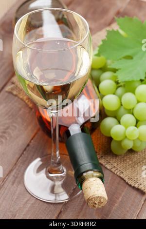 Vino bianco bicchiere, bottiglia e uva sulla tavola di legno Foto Stock