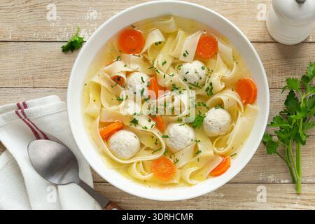 Polpette di pollo e zuppa di spaghetti di verdure in una ciotola bianca, vista dall'alto, sfondo in legno Foto Stock