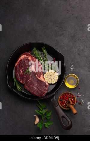 Bistecca di manzo crudo su teglia in ghisa nera, pronta per cucinare, sfondo nero, vista dall'alto, spazio per copiare Foto Stock